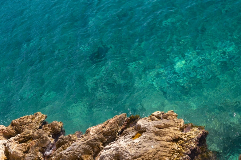 a man standing on top of a rock next to the ocean, by Simon Marmion, pexels contest winner, turquoise color scheme, banner, top - down photo, mediterranean