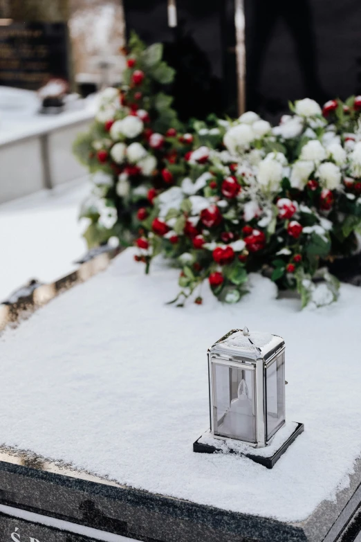 a small lantern sitting on top of a snow covered grave, by Julia Pishtar, flower decorations, side lights, exterior shot, multiple stories