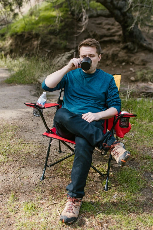 a man sitting in a chair drinking from a cup, camping, professional photo, liam, tall