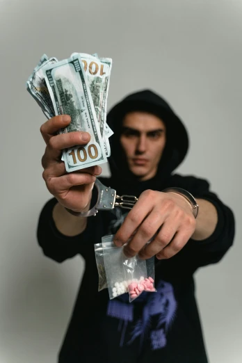 a man in a hoodie holding a bunch of money, an album cover, by Byron Galvez, pexels contest winner, handcuffed, 15081959 21121991 01012000 4k, male teenager, mdma