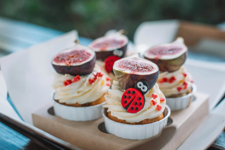 a white plate topped with cupcakes covered in frosting, by Julia Pishtar, trending on pexels, figuration libre, ladybug, on a hot australian day, botanicals, bakery