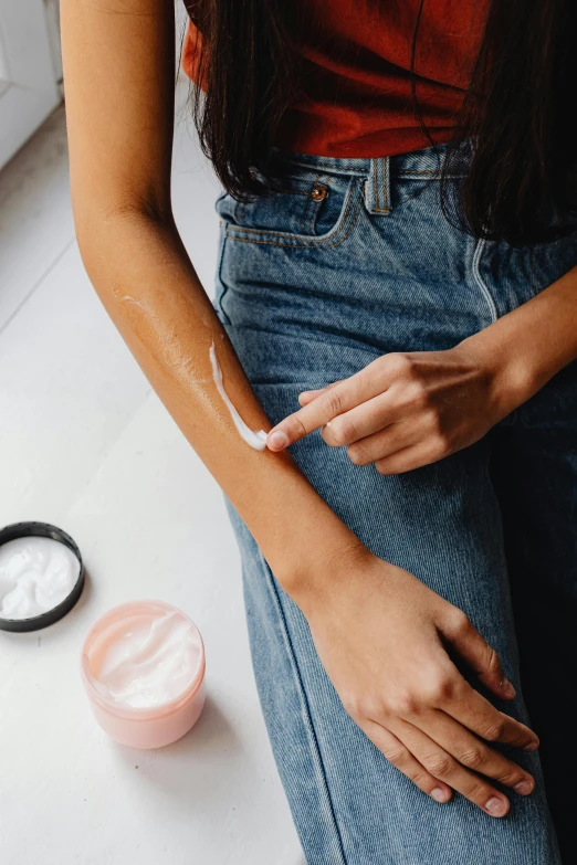 a woman sitting on a counter holding a jar of cream, a tattoo, by Olivia Peguero, trending on pexels, bandage on arms, goop, synthetic skin, textured base ; product photos