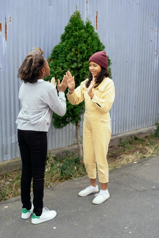 a couple of women standing next to each other, trending on pexels, happening, wearing track and field suit, reaching out to each other, yellow clothes, prompt young woman