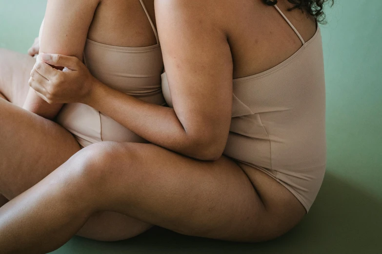 a woman sitting on the floor with her back to the camera, unsplash, muted colored bodysuit, woman holding another woman, manuka, thick lining