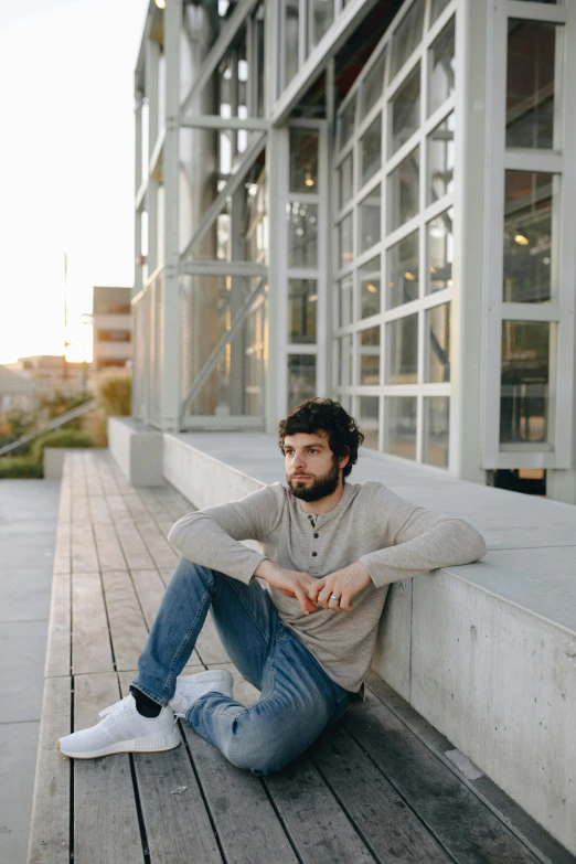 a man sitting on the ground in front of a building, by Adam Dario Keel, wearing casual sweater, thoughtful, wide full body, afternoon