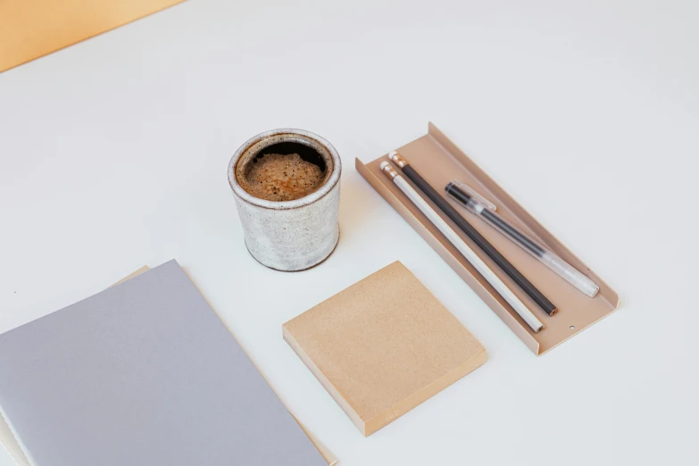a cup of coffee and a notebook on a table, inspired by Joseph Beuys, minimalism, inside its box, light grey, tungsten, birch
