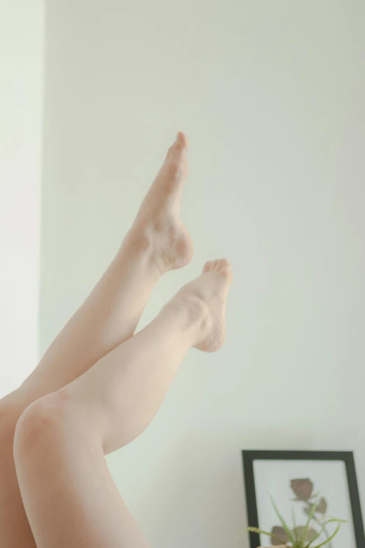 a woman laying on a bed with her legs up, unsplash, arabesque, pale!, standing on a shelf, soft pale tone, photo - realistic )