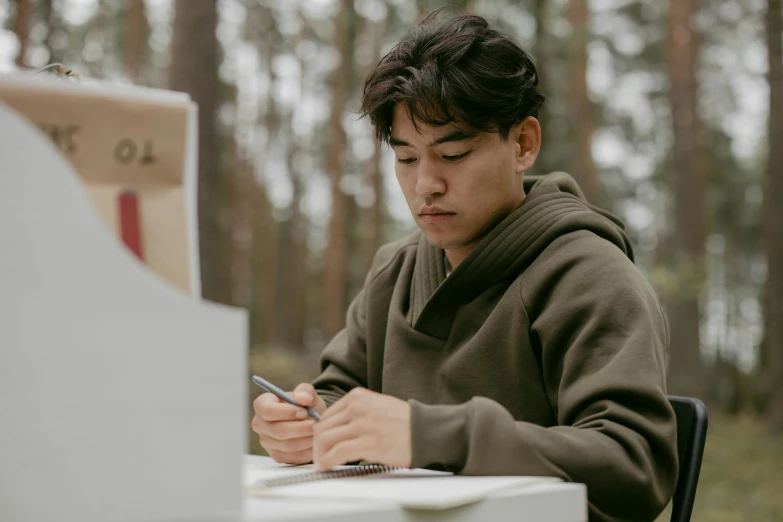 a young man sitting at a table using a cell phone, a drawing, by Emma Andijewska, pexels contest winner, in forest, korean writing, cardboard, concentrated look