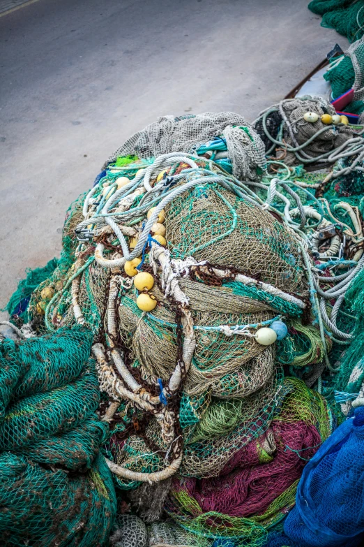 a pile of fishing nets sitting on the side of a road, a mosaic, sea - green and white clothes, dredged seabed, bangles, paul barson