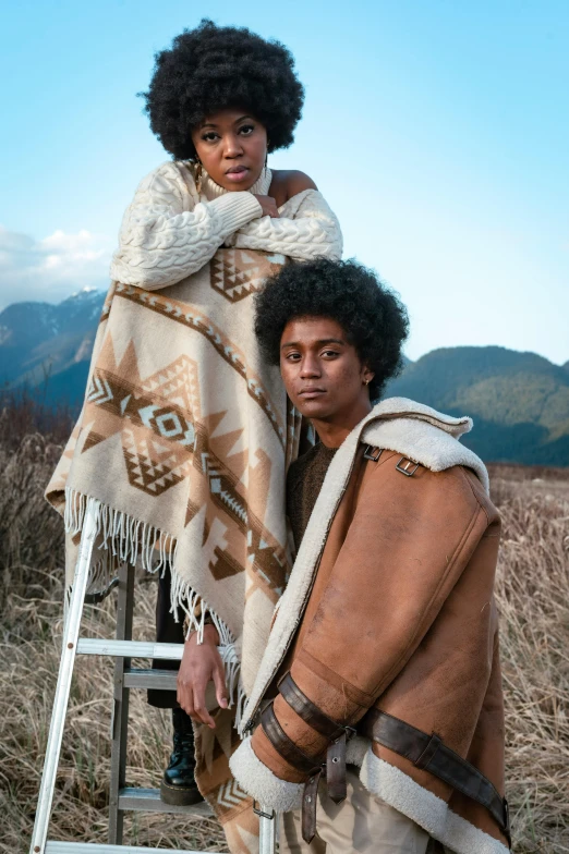 two women standing next to each other in a field, trending on pexels, black arts movement, covered with blanket, haida, fashion model features, caramel. rugged