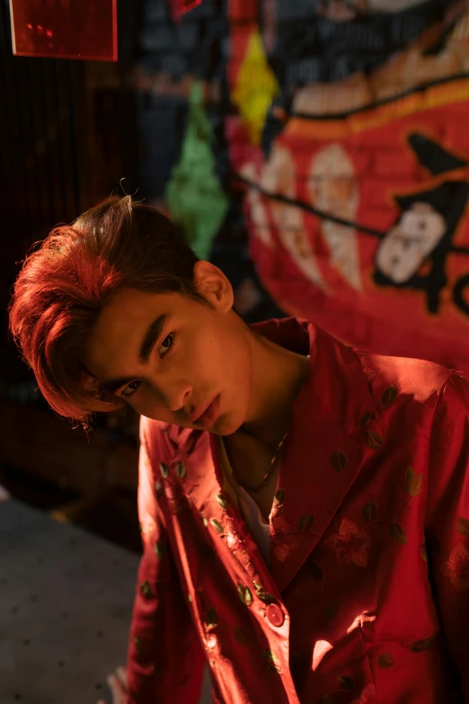 a man standing in front of a graffiti covered wall, an album cover, inspired by Zhang Han, trending on pexels, red dyed hair, red kimono, actor, ( ( theatrical ) )