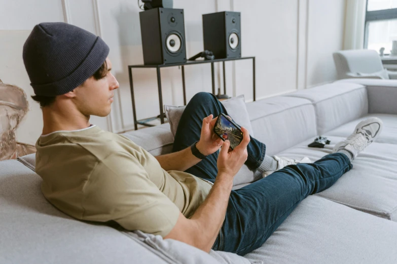 a man sitting on a couch holding a remote, an album cover, trending on pexels, gaming headset, avatar image, teenager hangout spot, looking at his phone