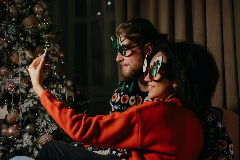 a man and woman sitting in front of a christmas tree, pexels contest winner, tech glasses, back facing the camera, gif, smartphone photo