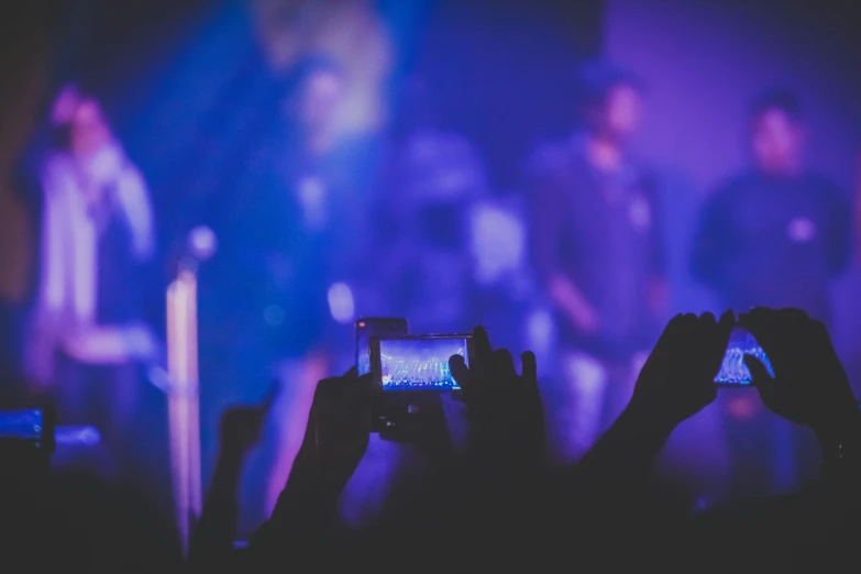 a group of people taking pictures with their cell phones, by Niko Henrichon, pexels, happening, cool purple slate blue lighting, rock musicians on the stage, hazy, looking across the shoulder