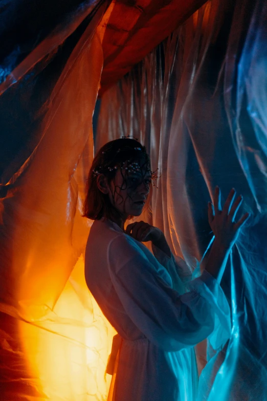 a woman standing in front of a curtain, a hologram, inspired by Elsa Bleda, pexels contest winner, conceptual art, blue and orange lighting, dressed in plastic bags, baba yaga, dressed as an oracle