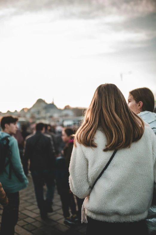 a group of people standing next to each other, trending on unsplash, arm around her neck, crowded square, rear-shot, woman holding another woman