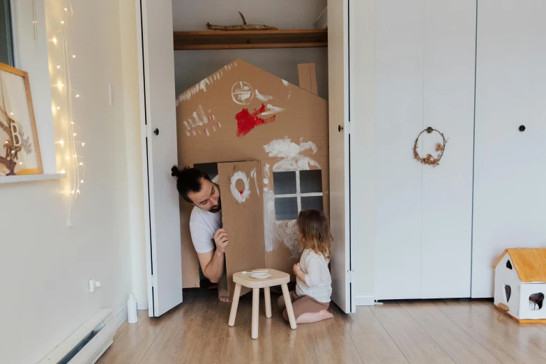 a woman and a child playing with a cardboard house, by Emma Andijewska, pexels contest winner, interior of a small, leaning on door, te pae, man