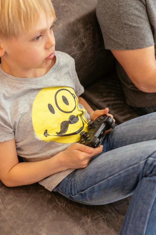 a little boy sitting on a couch playing a video game, inspired by Károly Brocky, happening, mustache and soul patch, wearing a modern yellow tshirt, smiley face, close - up photograph