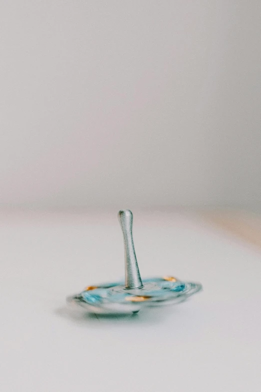 a glass candle holder sitting on top of a table, inspired by Lucio Fontana, unsplash, cloisonnism, sword and wand – water, light grey blue and golden, flying saucer, shallow depth of field