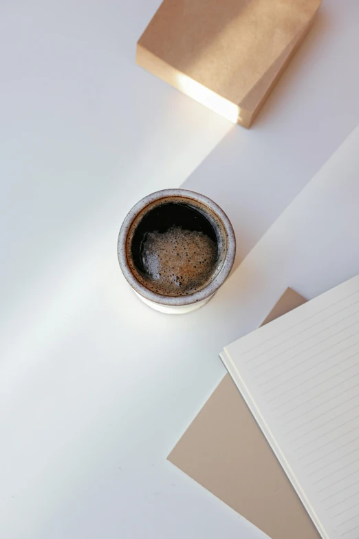 a cup of coffee sitting on top of a white table, by Robbie Trevino, process art, sustainable materials, background image, pot, on desk