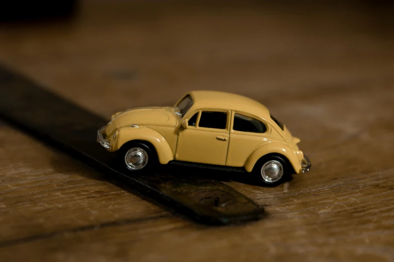 a toy car sitting on top of a wooden table, a macro photograph, by David Simpson, unsplash, yellow and charcoal leather, beetle, brown, kombi