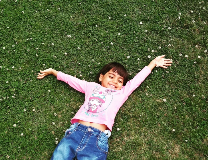 a little girl laying on top of a lush green field, pixabay, hurufiyya, pose(arms up + happy), avatar image, turkey, top - down photo