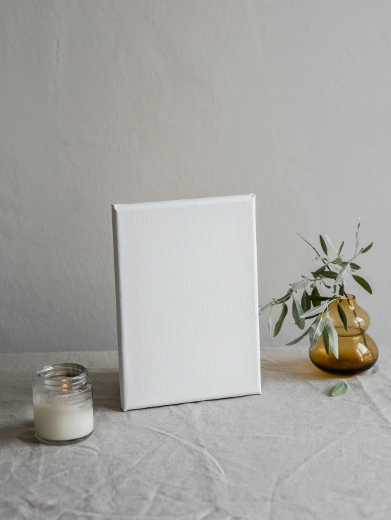 a picture frame sitting on top of a table next to a candle, a minimalist painting, unsplash contest winner, made of all white ceramic tiles, acrylic painting on oiled canvas, mid length portrait photograph, white cloth