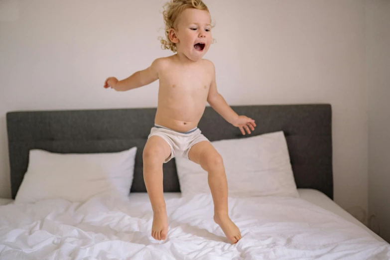 a toddler jumping on a bed with white sheets, happening, shirtless, bare thighs, having a good time, 5k