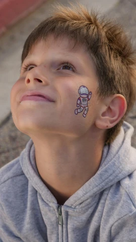 a young boy with a sticker on his face, a tattoo, by Sebastian Spreng, pexels, cute astronaut sticker art, high quality photo, thumbnail, celebration