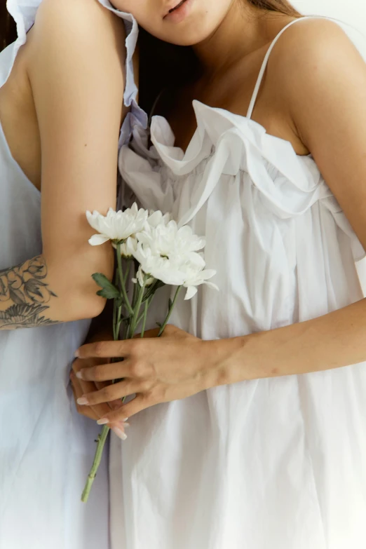 a woman laying in bed with a bouquet of flowers, a tattoo, by Matija Jama, trending on unsplash, romanticism, woman holding another woman, in a long white dress, lesbian embrace, holding daisy