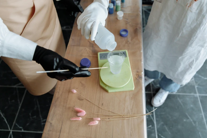 a group of people standing around a wooden table, scientific glassware, hot glue, high-quality photo, thumbnail