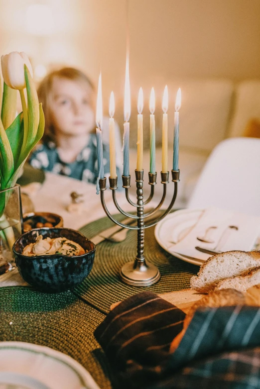 a little boy sitting at a table with a bunch of candles, a colorized photo, pexels, beautiful jewish woman, blue and gold color scheme, holiday season, bowl filled with food