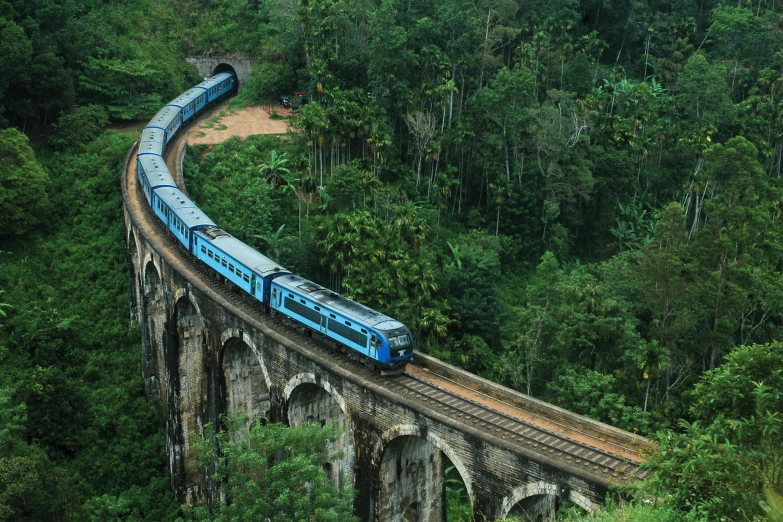 a large long train on a steel track, inspired by Steve McCurry, hurufiyya, archways made of lush greenery, blue, sri lankan landscape, ultra-high details