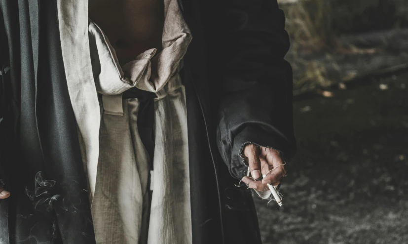 a close up of a person holding a cigarette, an album cover, inspired by Nicola Samori, unsplash, renaissance, grey tarnished longcoat, abigail larson, arcane clothing, hands of men