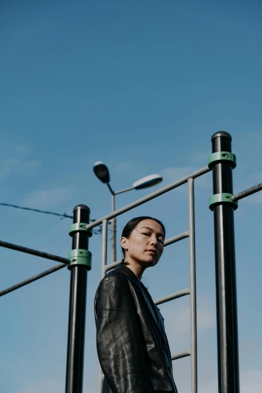 a man standing in front of a metal structure, inspired by Li Tiefu, unsplash, young asian woman, wearing leather, in a suburb, blue sky