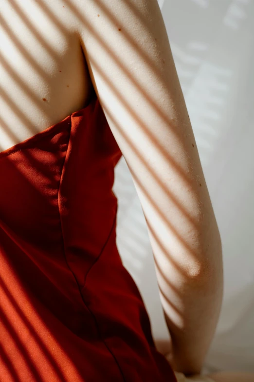 a woman in a red dress sitting on a bed, inspired by Elsa Bleda, trending on pexels, detailed shadows, showing her shoulder from back, soft silk dress, soft sunbeam