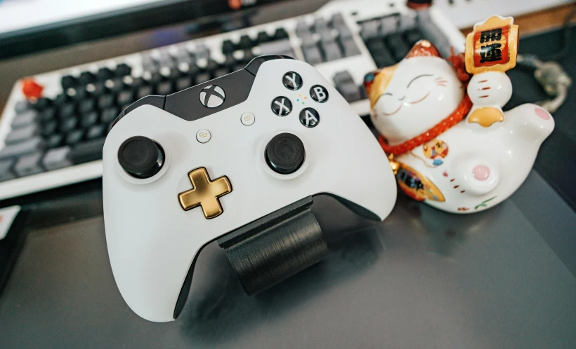 a white controller sitting on top of a desk next to a keyboard, by Julia Pishtar, liquid gold, x - box, cuphead, gtr xu1