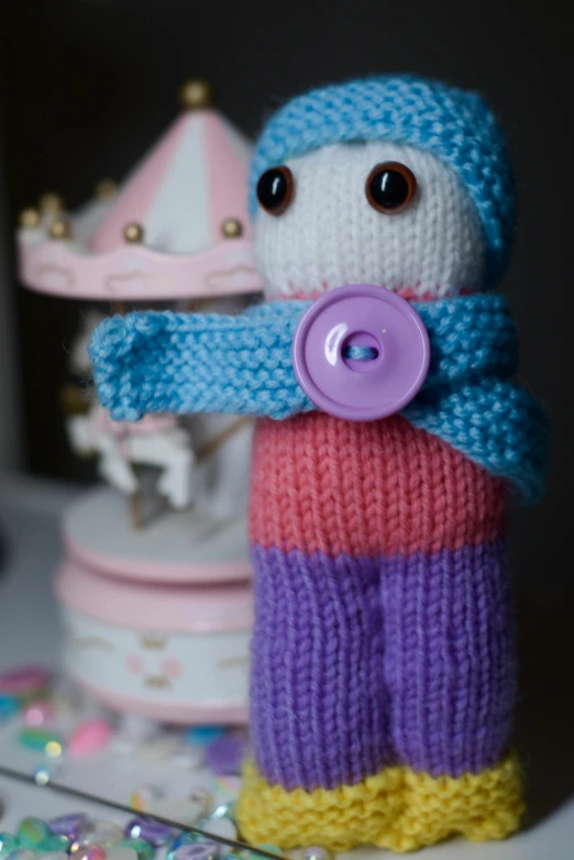 a close up of a stuffed animal on a table, blue and purple, toy camera, knitted hat, humanoid servo