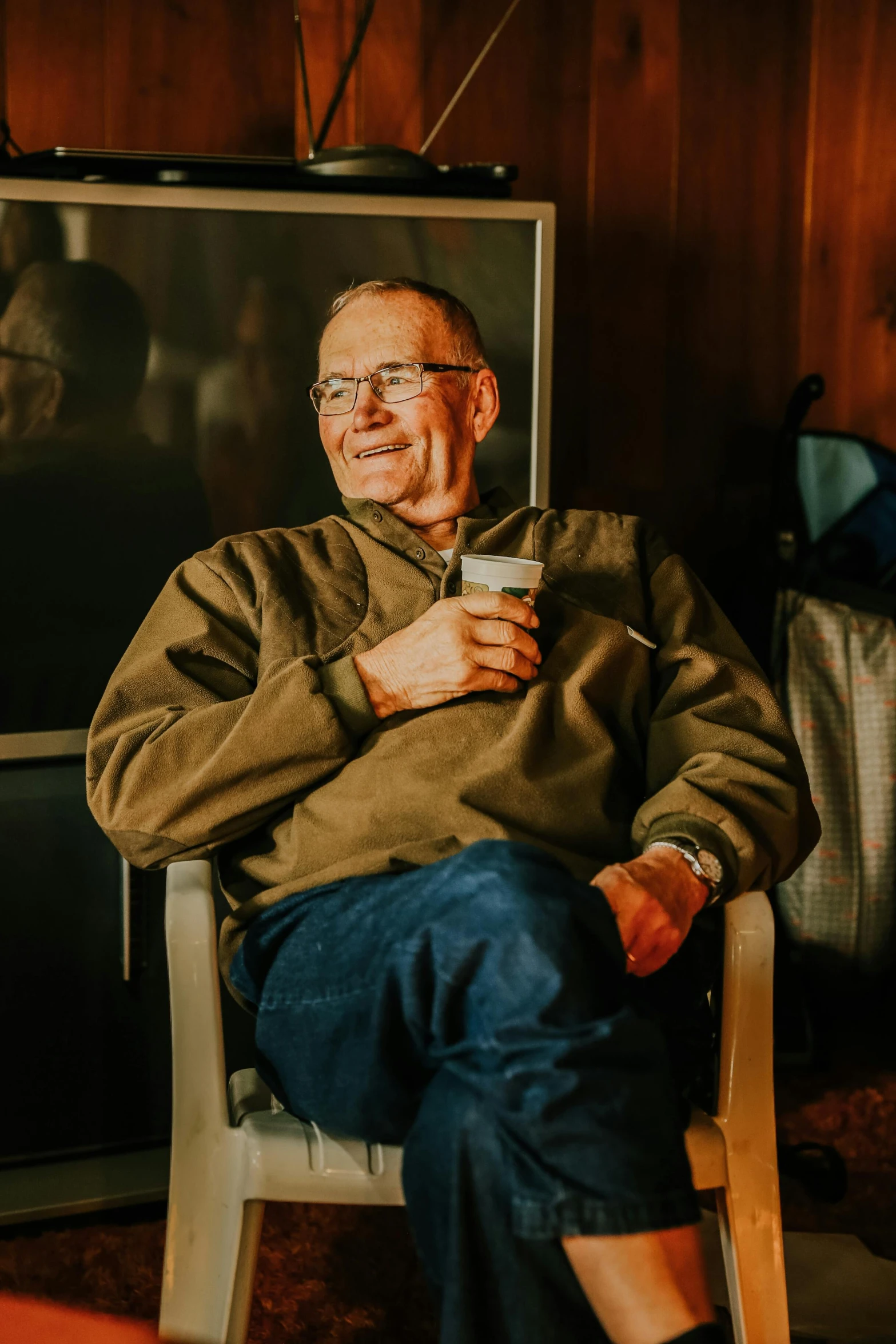 a man sitting in a chair in front of a television, a portrait, by William Berra, pexels contest winner, holding a mug of beer, jim cornette, in a cabin, profile image