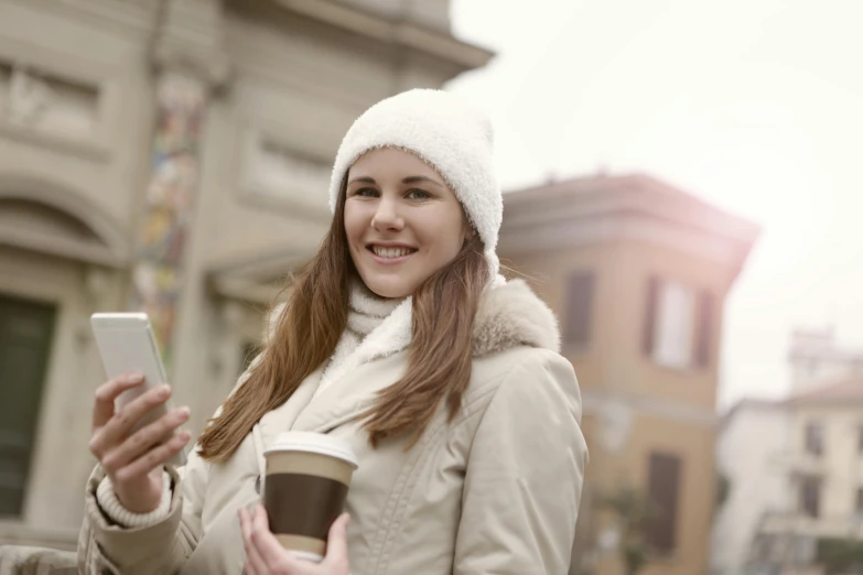 a woman holding a cup of coffee and a cell phone, a picture, by Sebastian Vrancx, shutterstock, happening, beanie, italian, college students, 3945074687