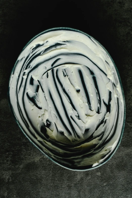 a bowl of cream sitting on top of a table, inspired by Joris van der Haagen, mysterious black slime, marbled swirls, no cropping, close-up from above