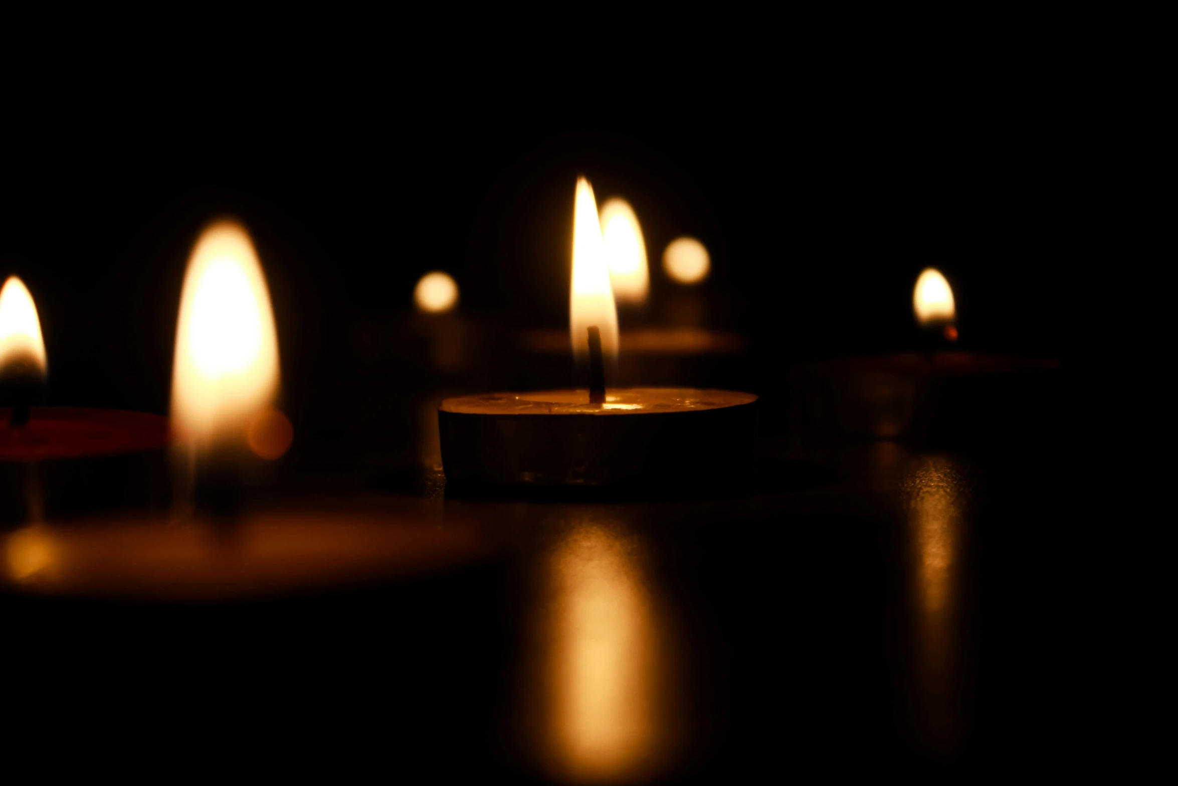 a group of lit candles sitting on top of a table, with a black background, lynn skordal, lit from the side, calm feeling