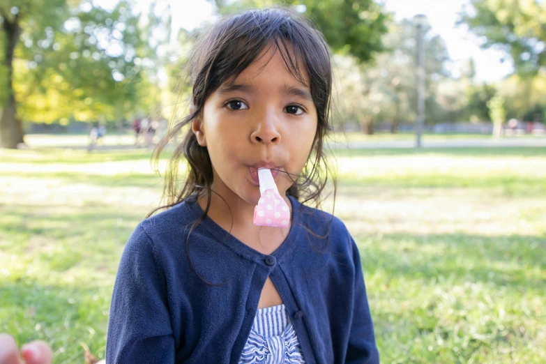 a little girl eating a popsicle in a park, by Sven Erixson, pexels contest winner, sydney park, bubble gum, manuka, looking to camera
