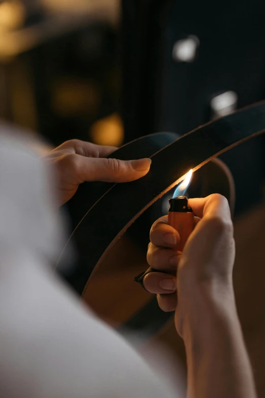 a person holding a lighter in their hand, an album cover, by Adam Marczyński, trending on pexels, working in the forge, leather straps, lighting her with a rim light, lacquerware