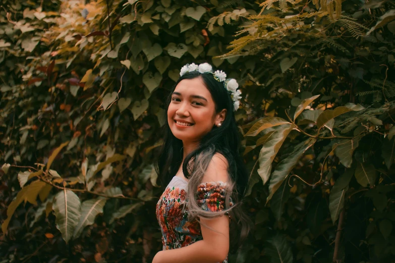 a woman standing in front of a bush with flowers in her hair, inspired by reyna rochin, pexels contest winner, sumatraism, smiling girl, avatar image, 18 years old, patterned clothing