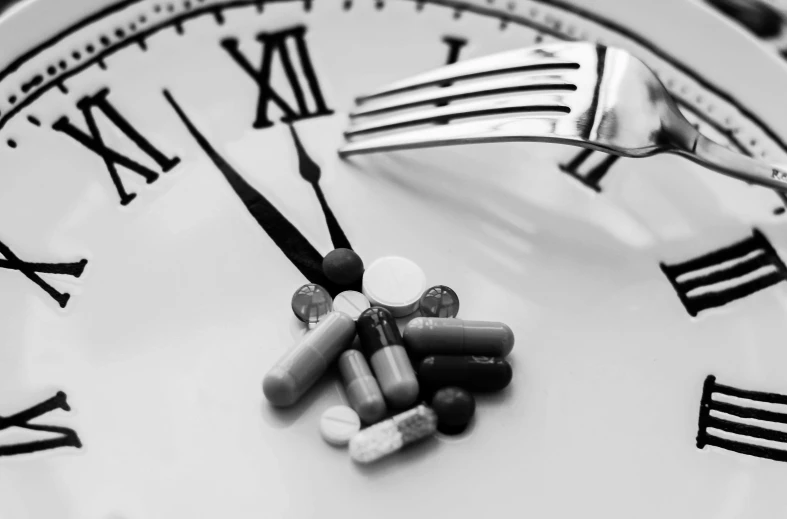 a plate with a fork and some pills on it, a black and white photo, by Kristian Zahrtmann, pexels, giant clock, photorealistic shot, chemical substances, slightly blurred