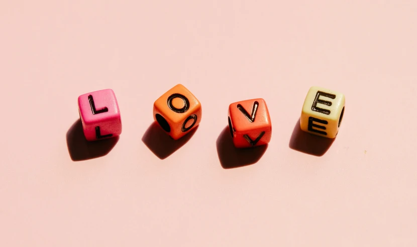 three dice with the word love spelled on them, by Olivia Peguero, trending on pexels, pink and orange, beads, jen atkin, for vogue