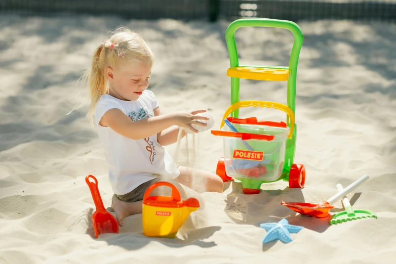 a little girl playing in the sand with toys, cart, as well as the handyboy, monika, ready to eat