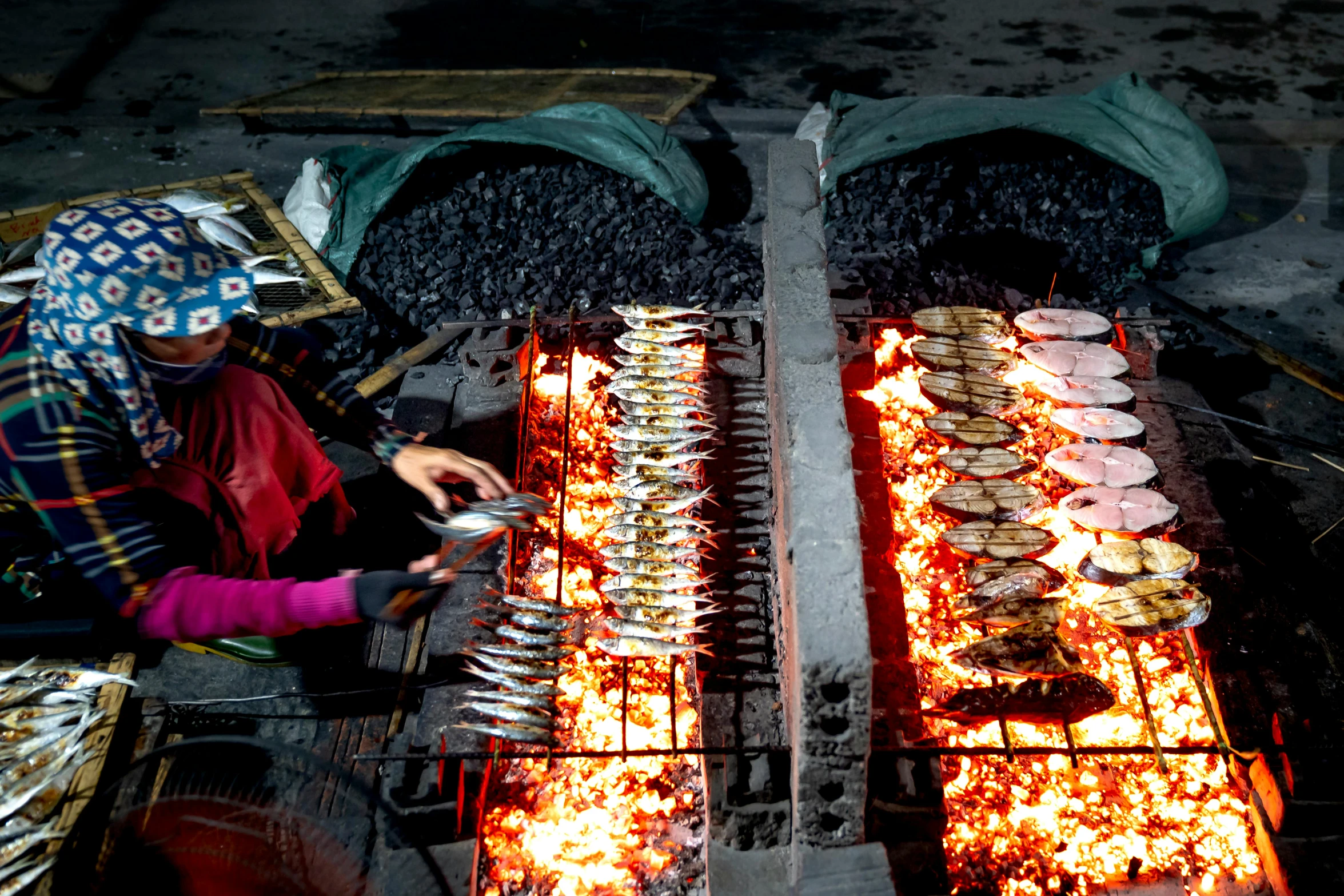 a woman is cooking food on a grill, by Julia Pishtar, pexels contest winner, hurufiyya, fish seafood markets, hangzhou, avatar image, night photo