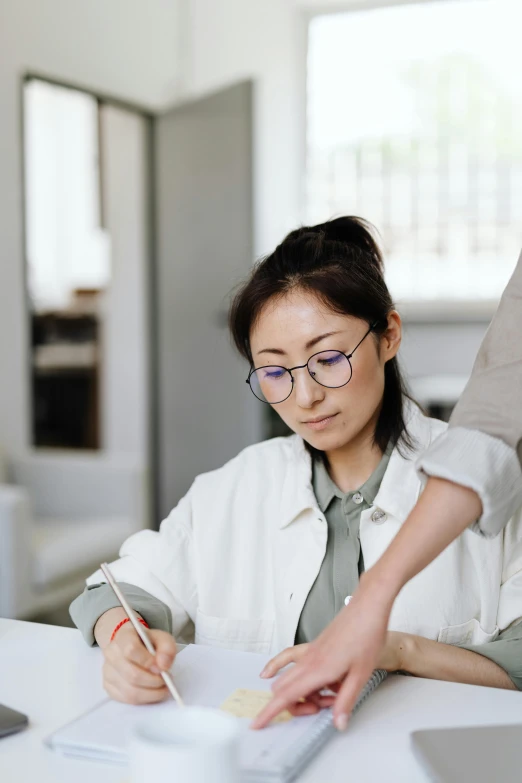 a woman sitting at a desk in front of a laptop, by Jang Seung-eop, trending on pexels, academic art, two people, ethnicity : japanese, grey, writing on a clipboard